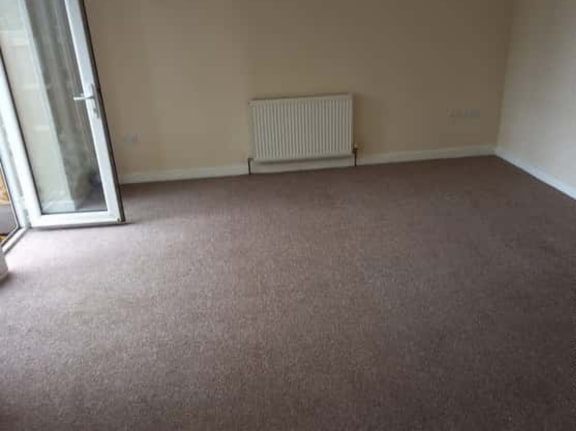 This is a photo of a living room after it has been cleaned. The room is empty and has a brown carpet that has been steam cleaned works carried out by Mile End Carpet Cleaning